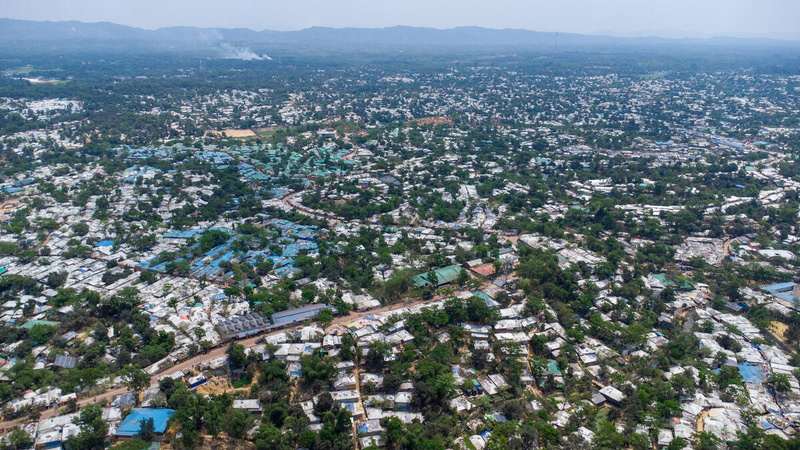 An aerial view of a vast refugee settlement with shelters extending to a mountainous horizon
