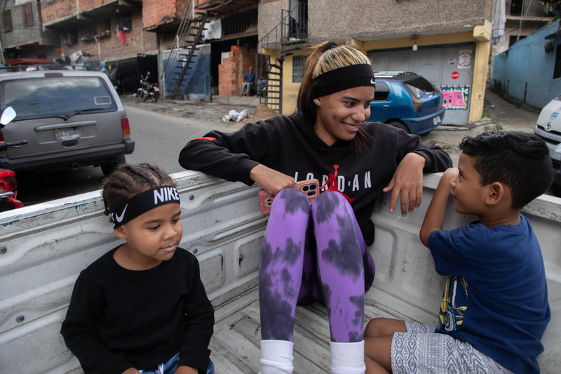 A woman and two young boys sit in the flatbed of a white truck driving along a city street