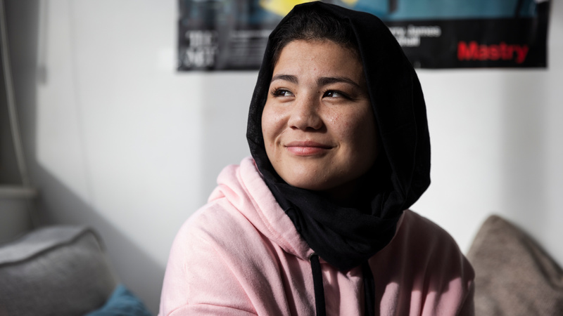 A young smiling woman in a pink hoodie and a black head scarf.