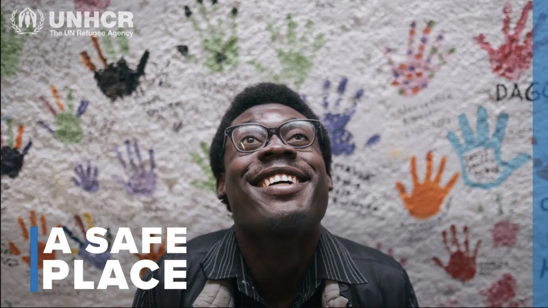 A portrait of a man in front of a wall covered in colourful handprints.
