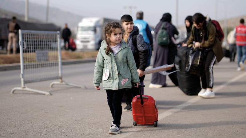 A young child walks on asphalt pulling a small suitcase.