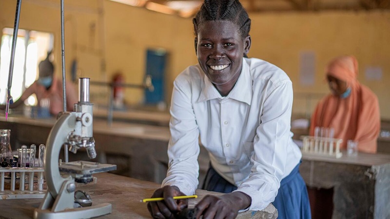A young woman in a science classroom smiles for the camera. 