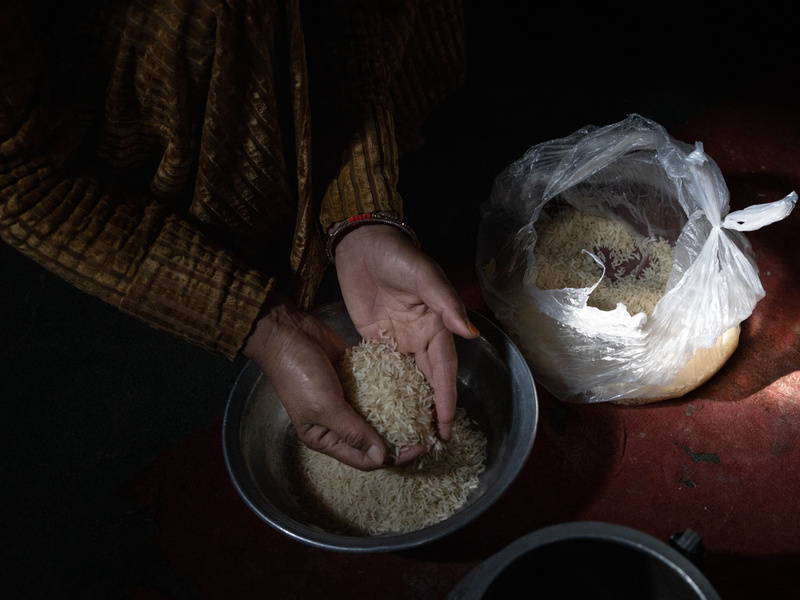 A woman's hands hold a handful of rice above a metal bowl.