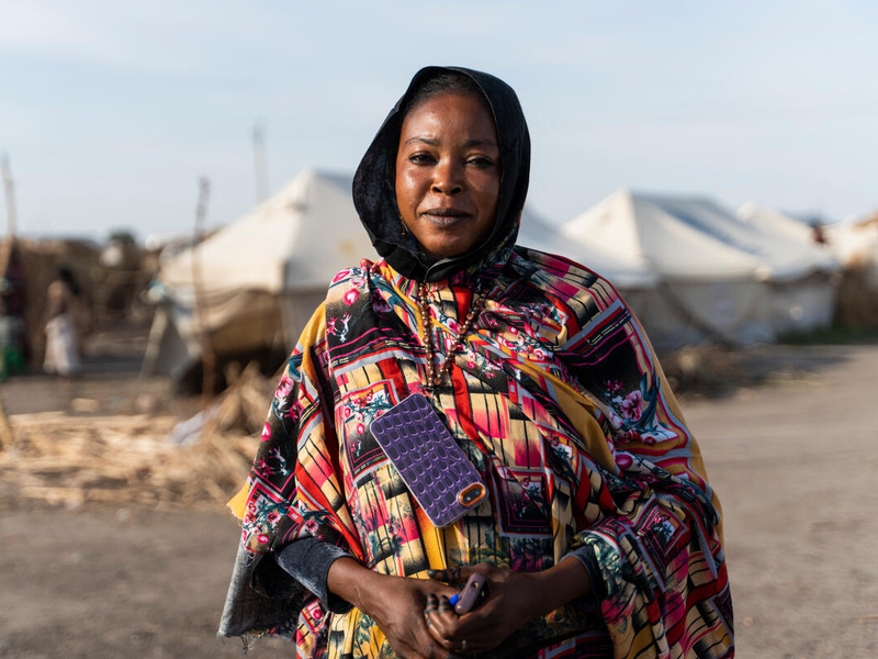 A woman in a colourful dress stands in front of rows of white tents in an IDP camp.