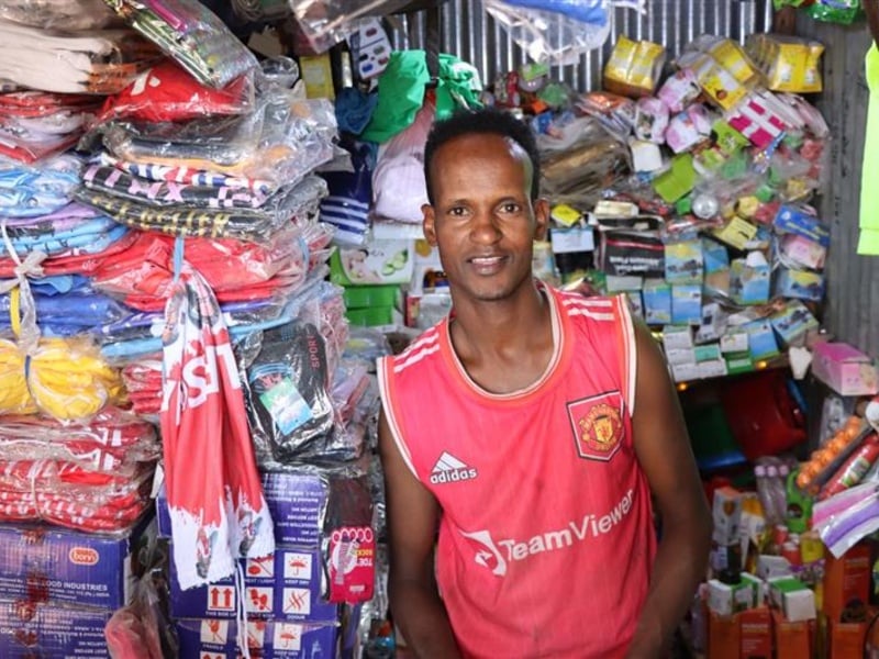 A young man standing in front of a shop full of various supplies.