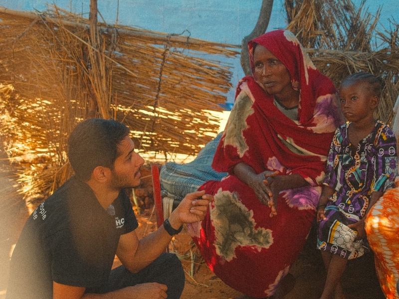 Omar sitting on the ground and speaking with a Sudanese family