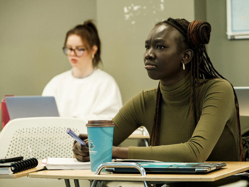 Mary Makes sits at a desk in a classroom.