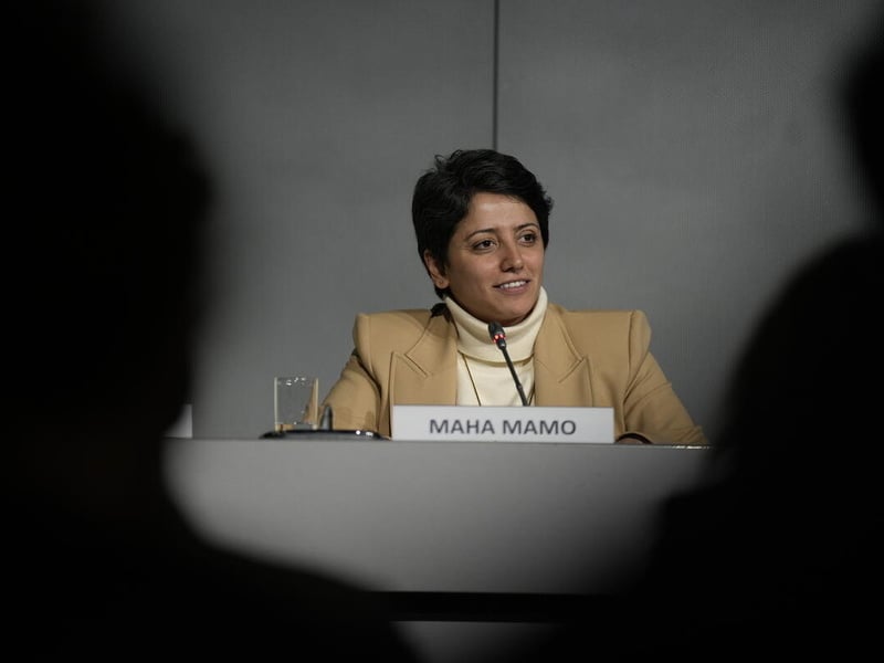 Formally stateless person Maha Mamo speaks at a panel during the Global Refugee Forum 2023. She is seated at a table, with the silhouettes of audience members framing the scene.