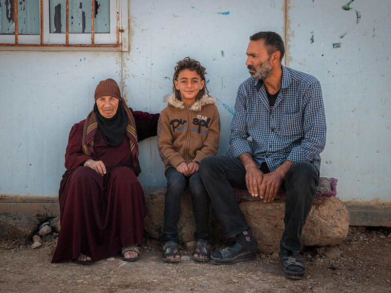 جدة سورية وابنها وحفيدها يجلسون معاً على مقعد في مخيم الزعتري للاجئين.