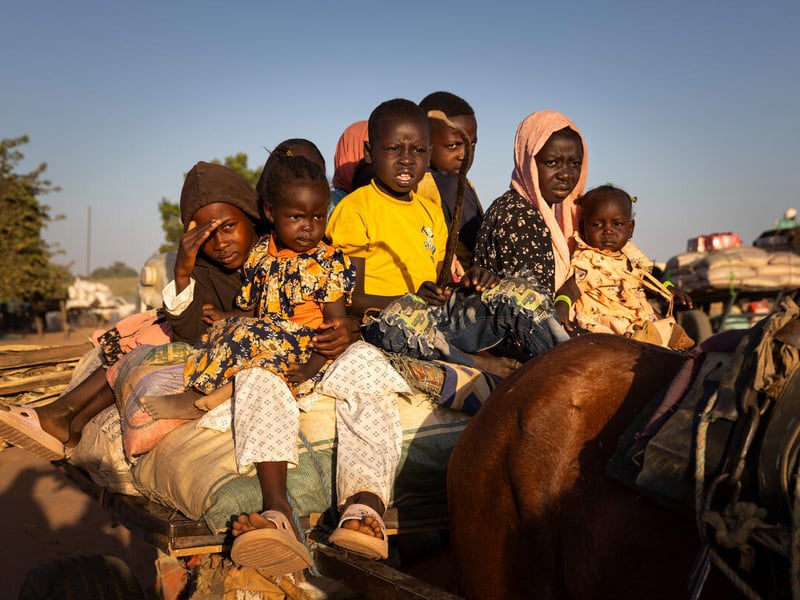 A group of Sudanese children sit on top of a cart behind a horse.