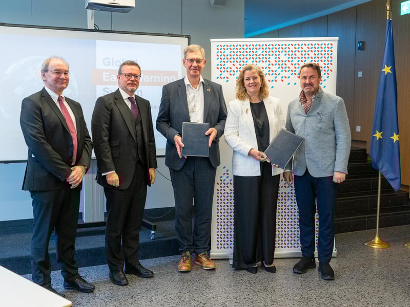 Four men and one woman stand looking at the camera while holding up two documents