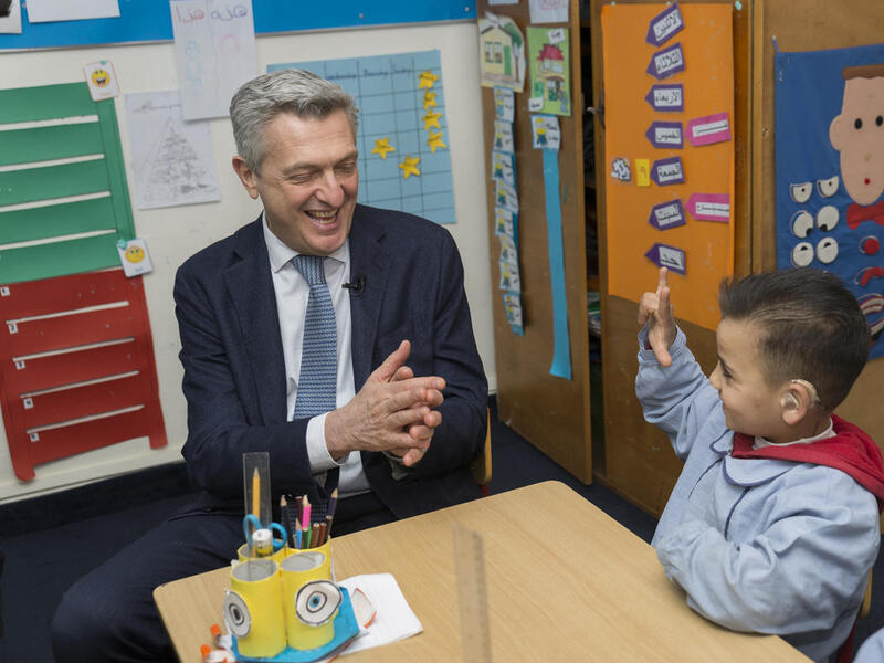 UNHCR High Commissioner Filippo Grandi sits with a 7-year old Syrian refugee child in a classroom. The child is wearing a hearing aid.