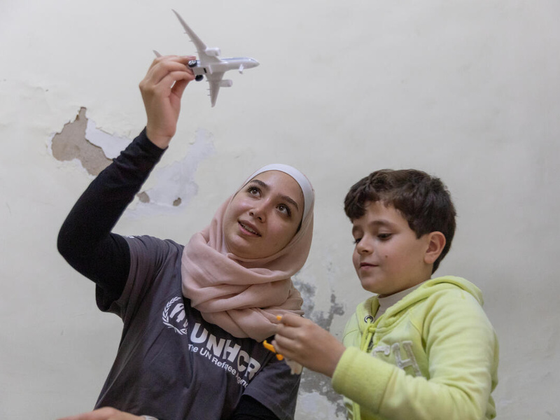 A young woman plays with a young boy with a plane toy.