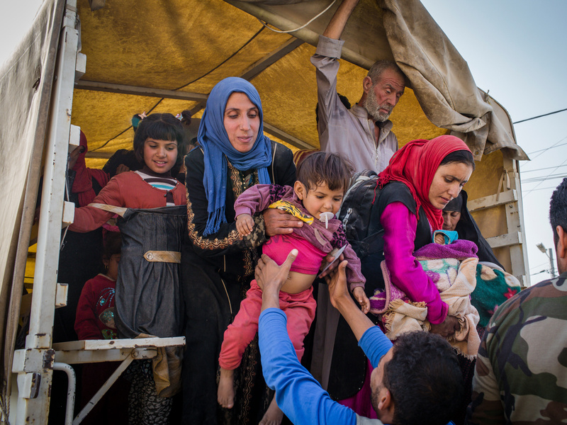 Iraqi men, women and children climbing down from a truck