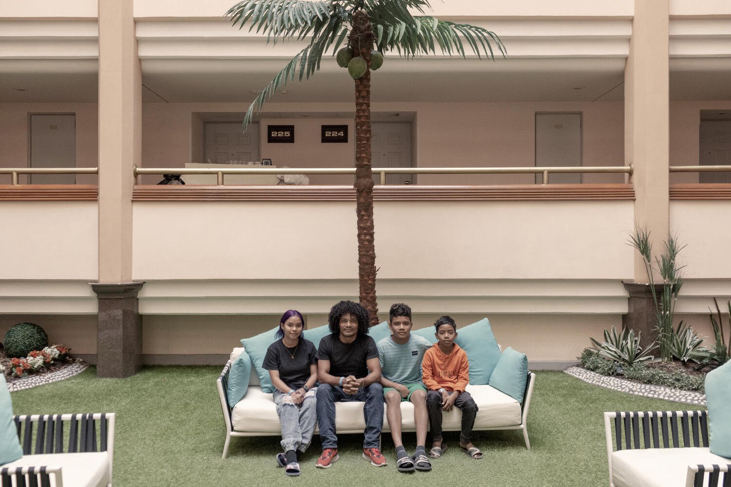 A man sits on a couch in a hotel with his three children. 