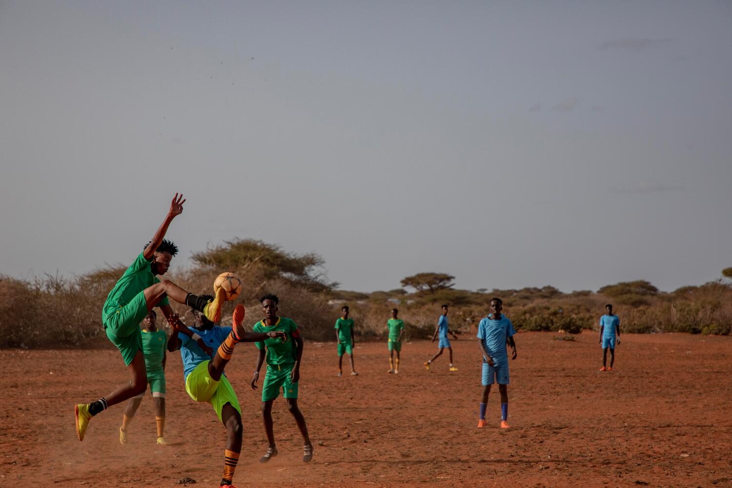 Two players compete for the ball during a soccer game on a dusty pitch.