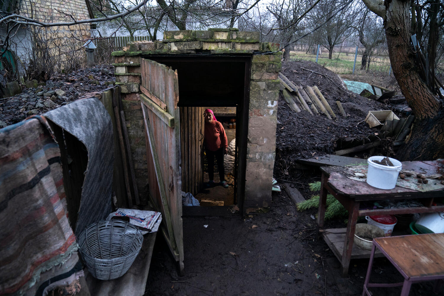 A woman stands in the doorway of an underground root cellar in her back yard.