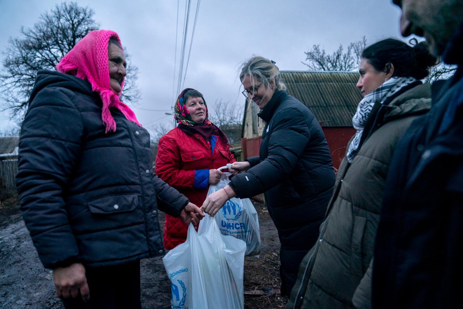Two Ukrainian women receive bags of food and other aid items from members of UNHCR staff.