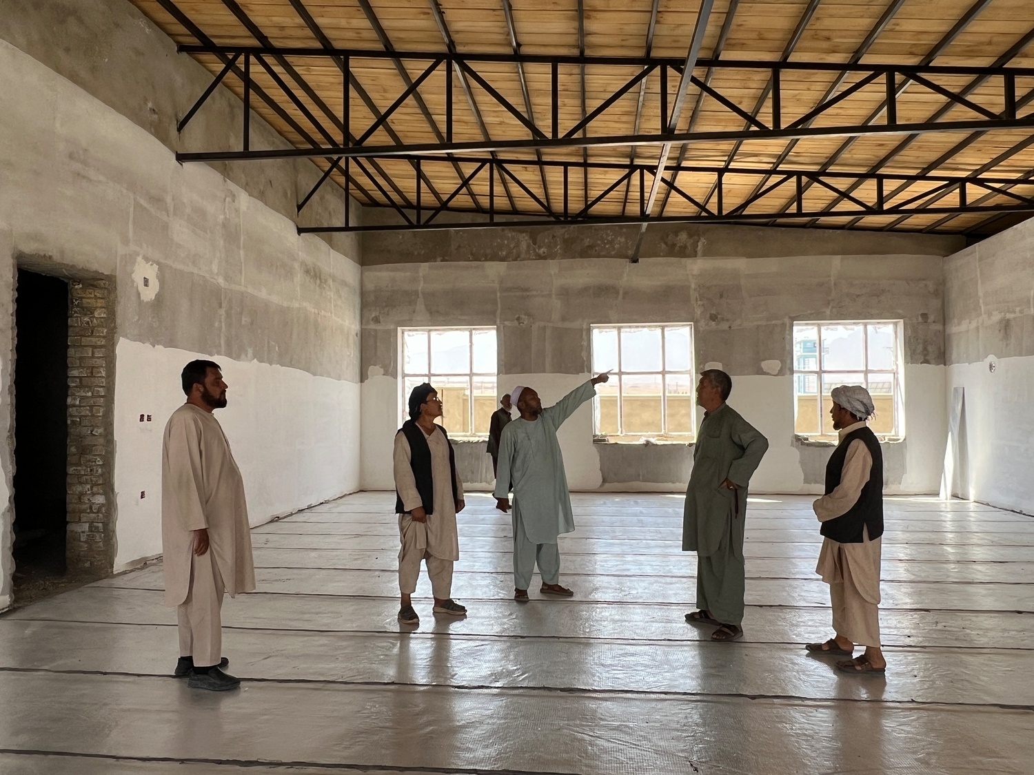 Five man stand in a nearly completed building. A man in the centre is pointing to something off camera.