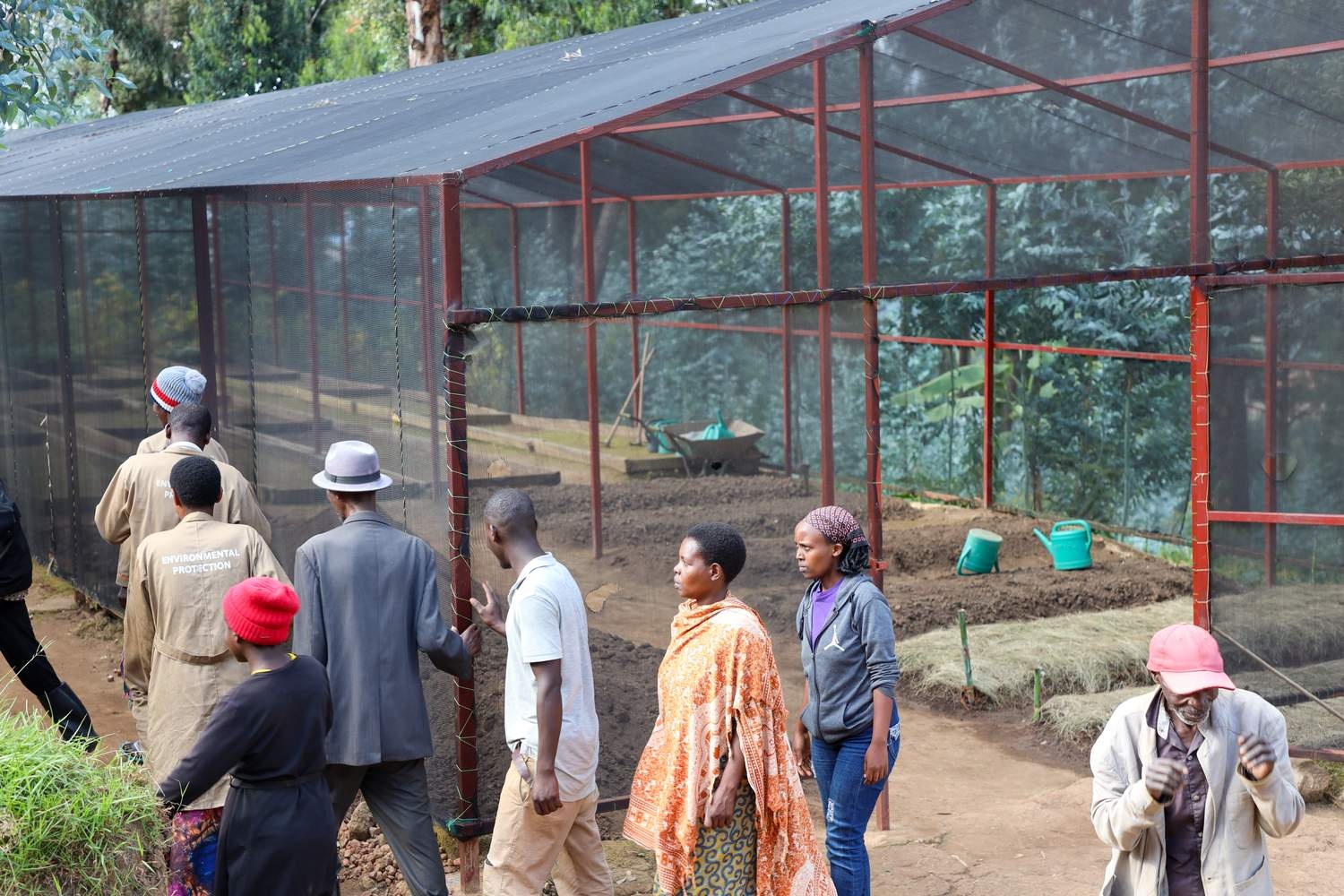 Men and women outside a shaded mesh greenhouse.