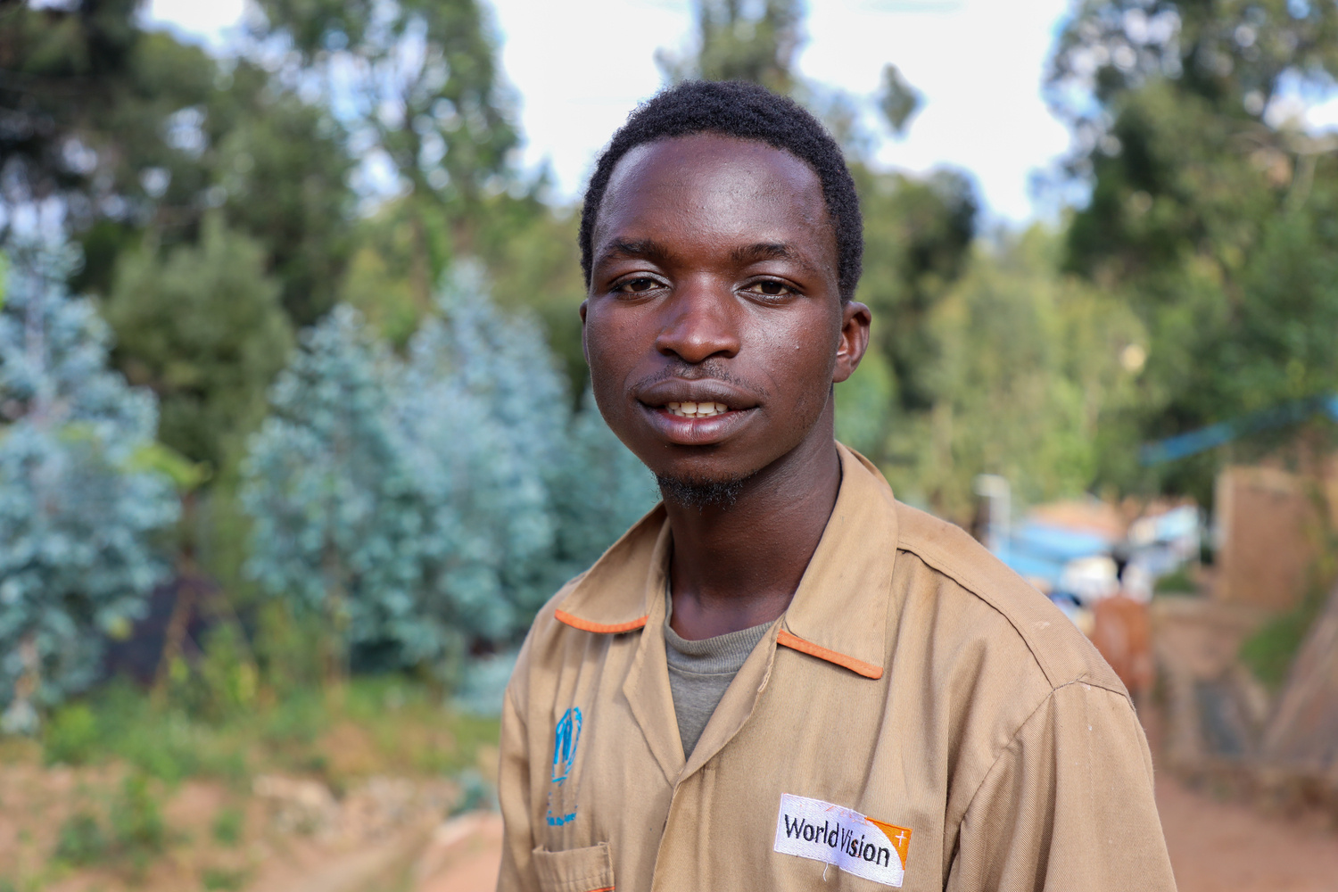 A young man in a brown shirt stands in a tree nursery in a refugee camp in Rwanda.