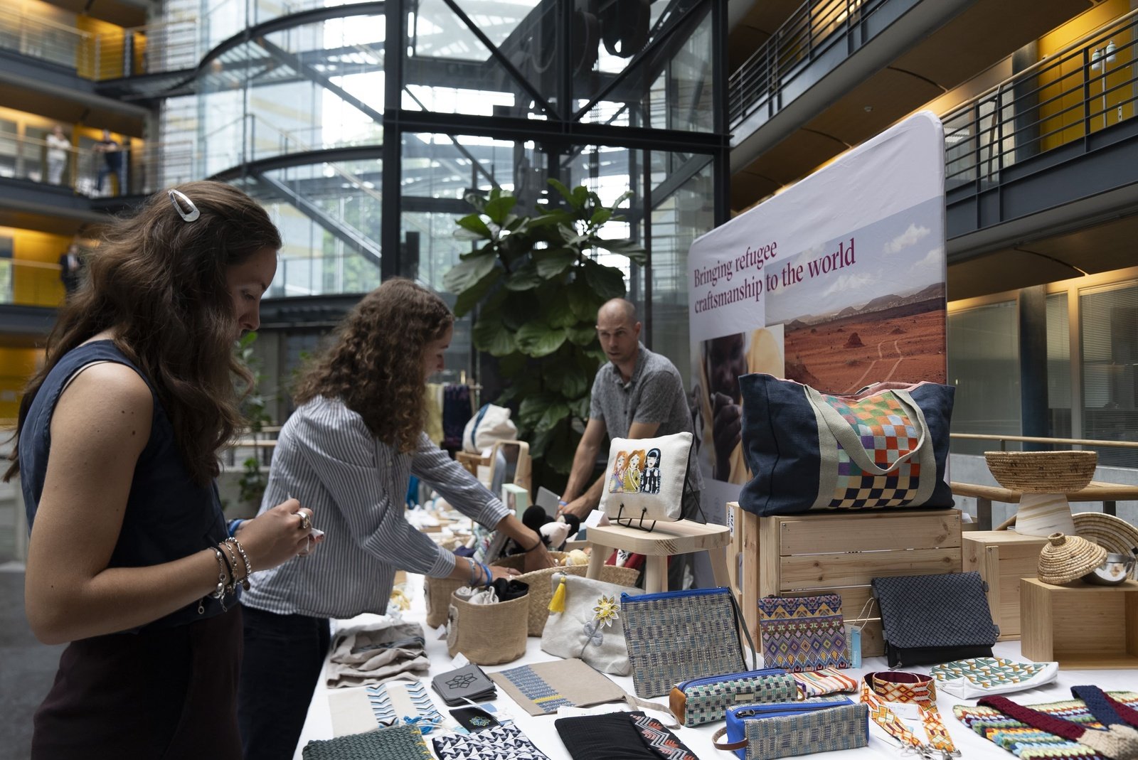 Two women browse handicraft items at a stall in the lobby of an office building