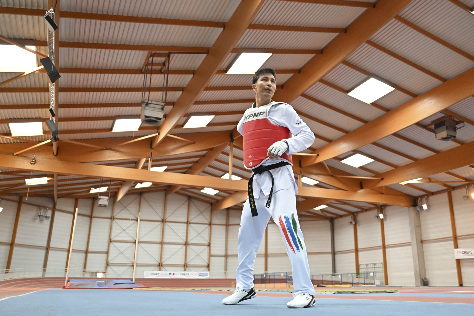 Un homme en uniforme de taekwondo se tient dans un gymnase.