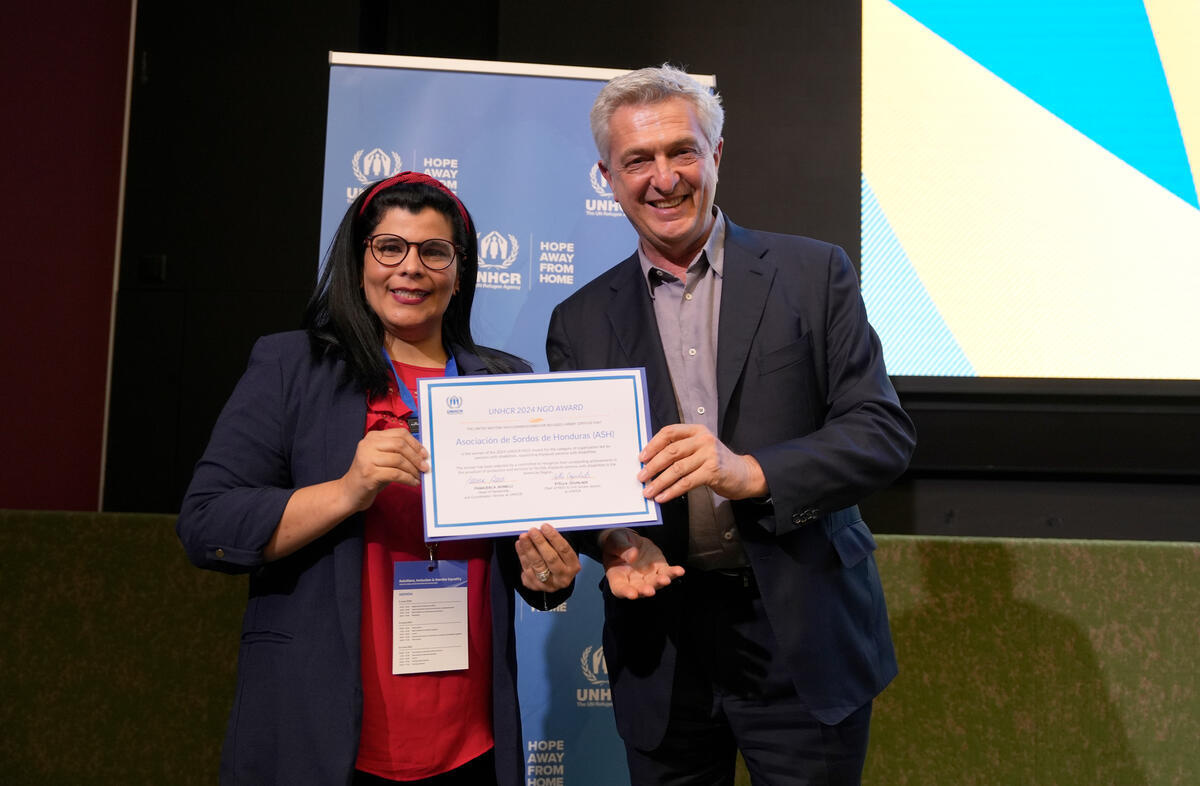 Ms. Estefani Claros Madrid and United Nations High Commissioner for Refugees Filippo Grandi holding up an award and smiling at the camera