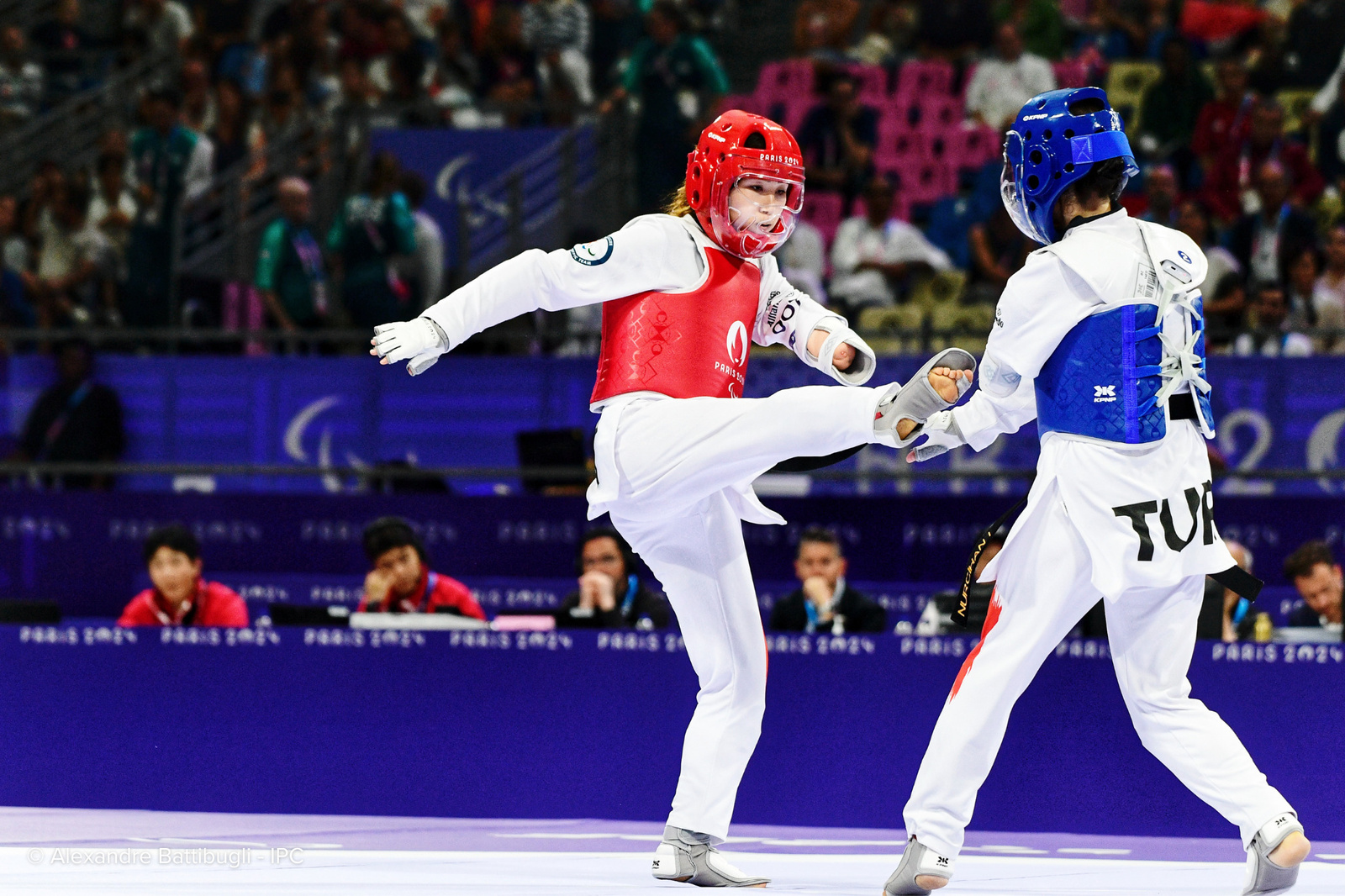 A taekwondo athlete wearing red pads aims a kick at her opponent in blue.