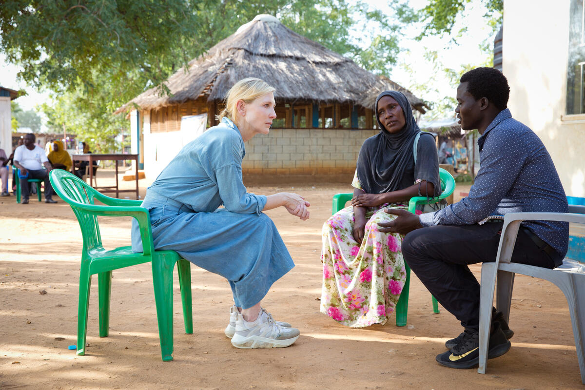 Cate deep in conversation with two refugee students, seated outside. A hut is in the background.