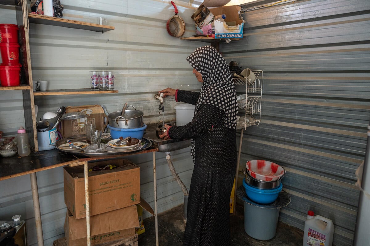 A woman stands inside the kitchen of her shelter as she washes dishes.