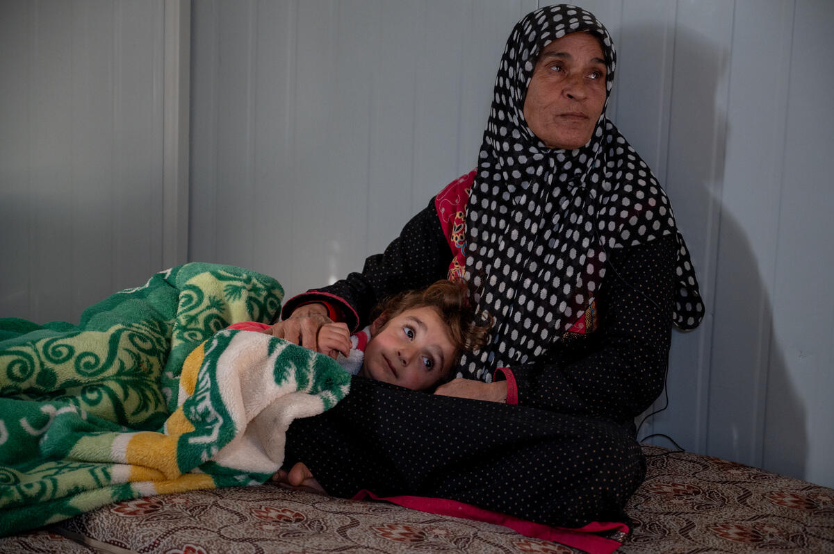 A woman sits in her shelter as her five-year-old granddaughter sleeps on her lap, covered with a blanket.