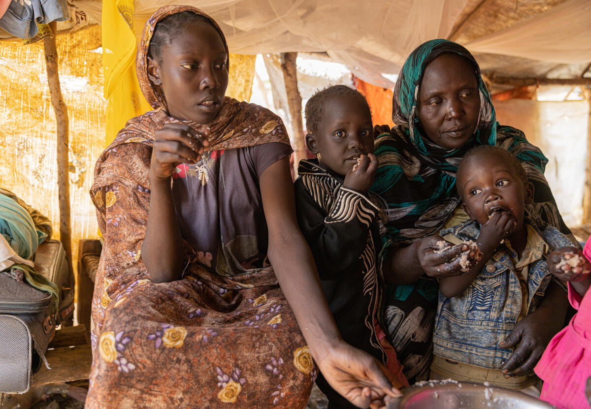 A woman and her daughters and nephew eat together inside a shelter