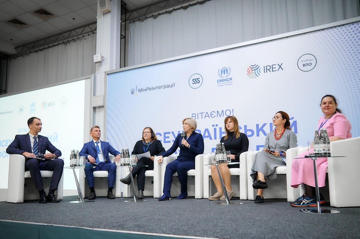A group of seven people speaking on a panel at a forum
