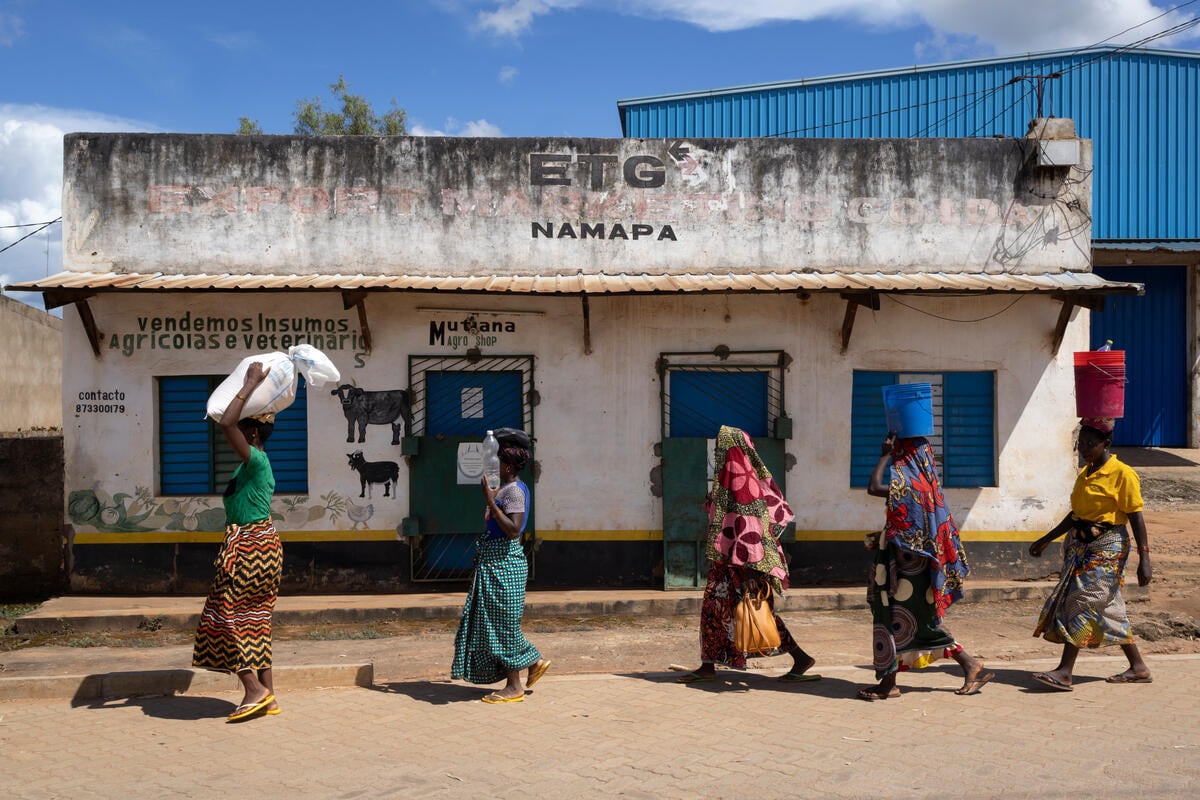 Cinq femmes passent devant un magasin fermé en portant des provisions sur la tête.