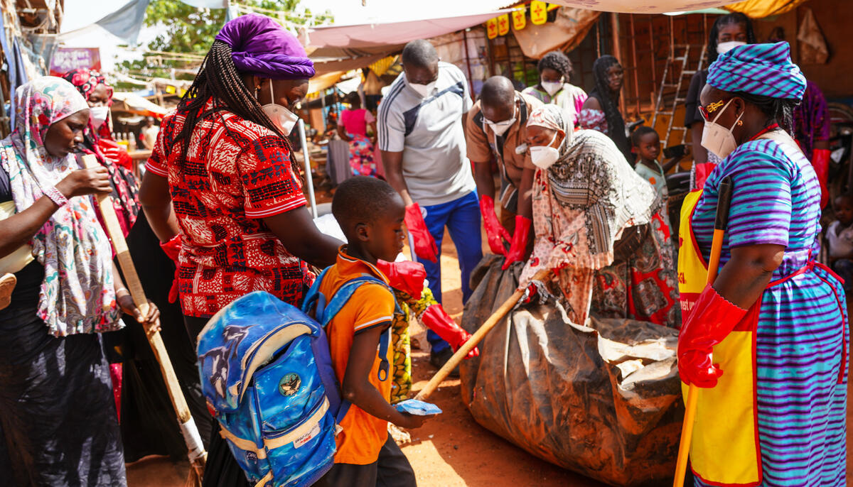 A group of colourfully dressed refugees help to clean an outdoor market.