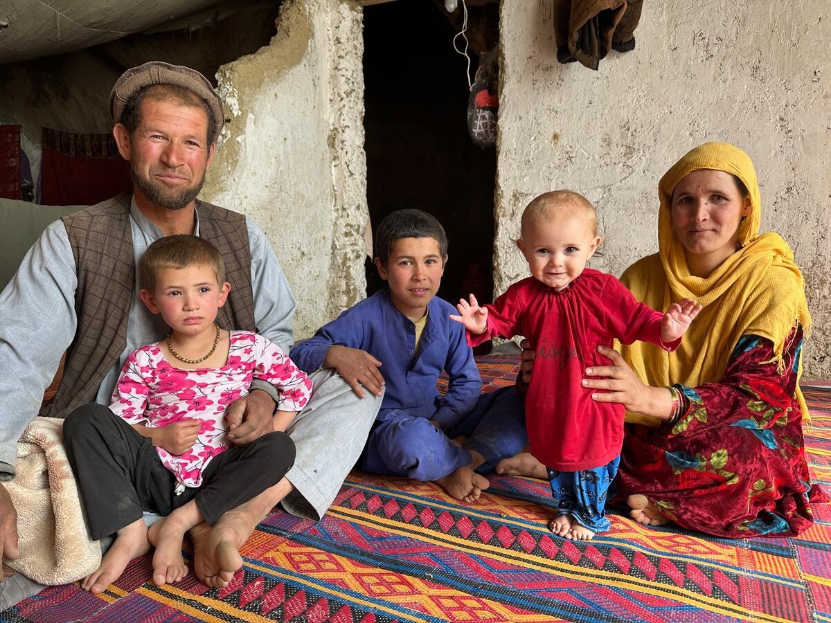 A man and his wife and their three children sits on a mat in their house as they pose for a photo