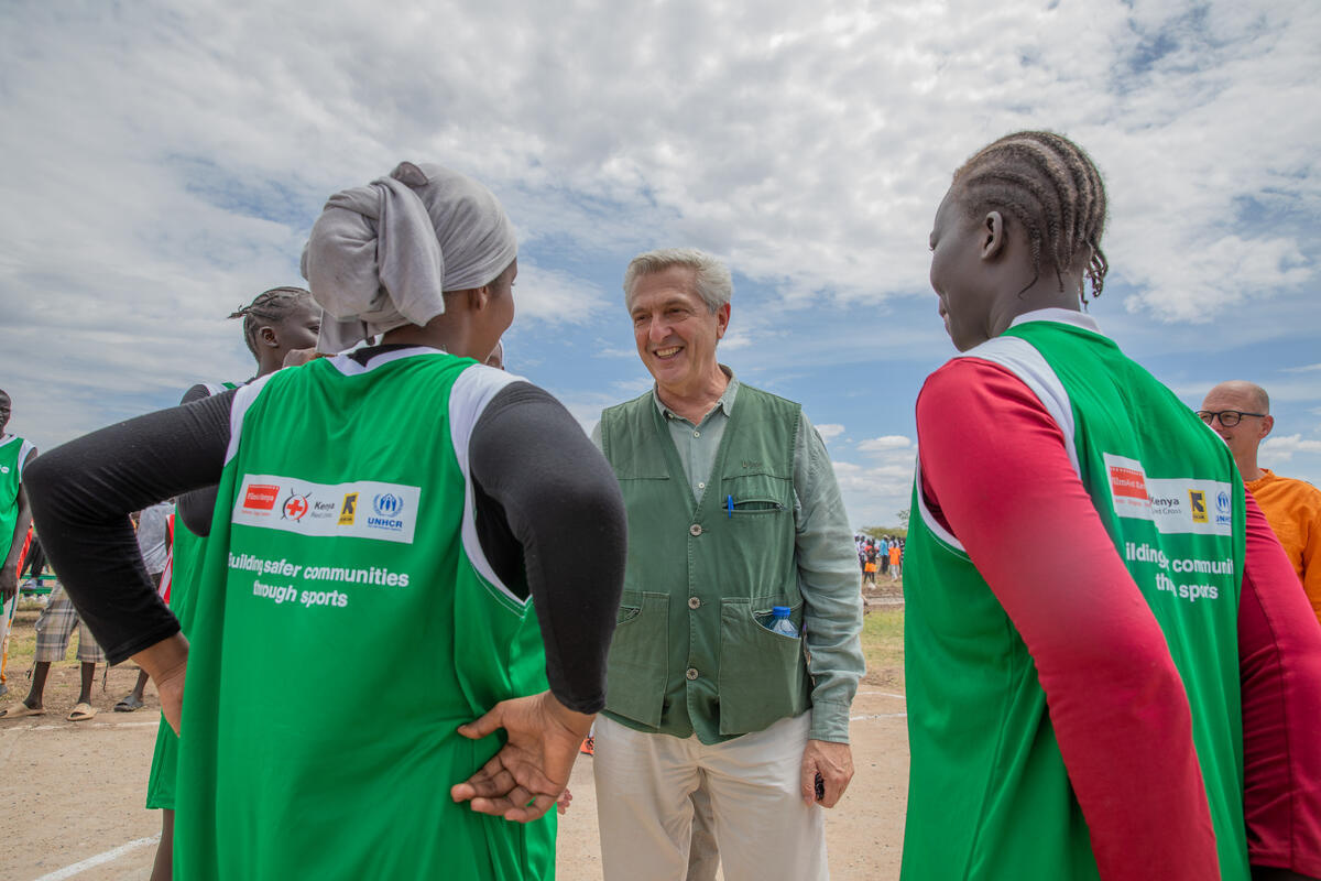 A man in a green vest talks to two young women with their backs to the camera.