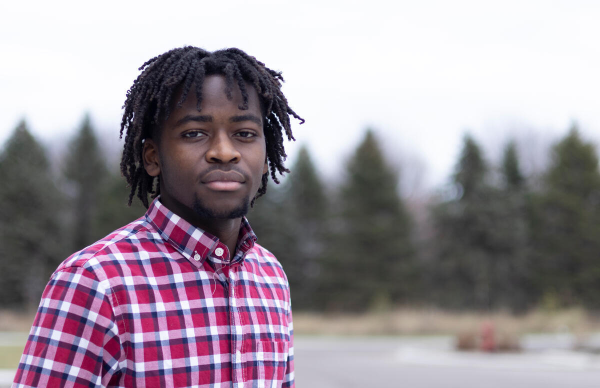 A young man with braided hair looks into the camera as he poses for a photo.