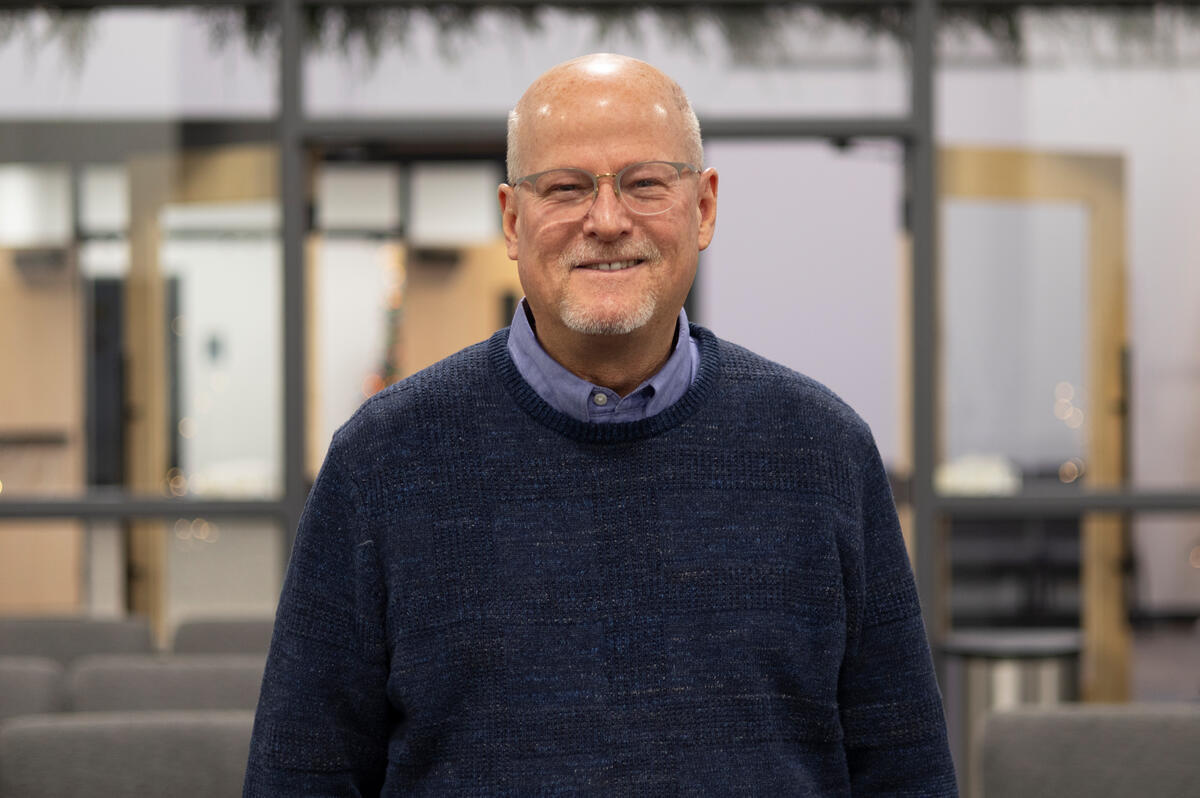 A spectacled pastor poses for a photo, smiling. 