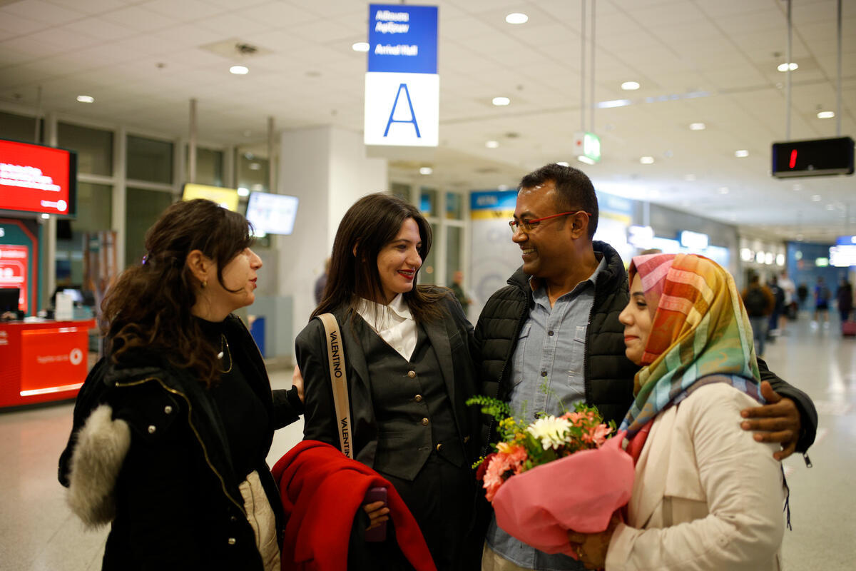 Three women and a man smile and embrace at an airport.