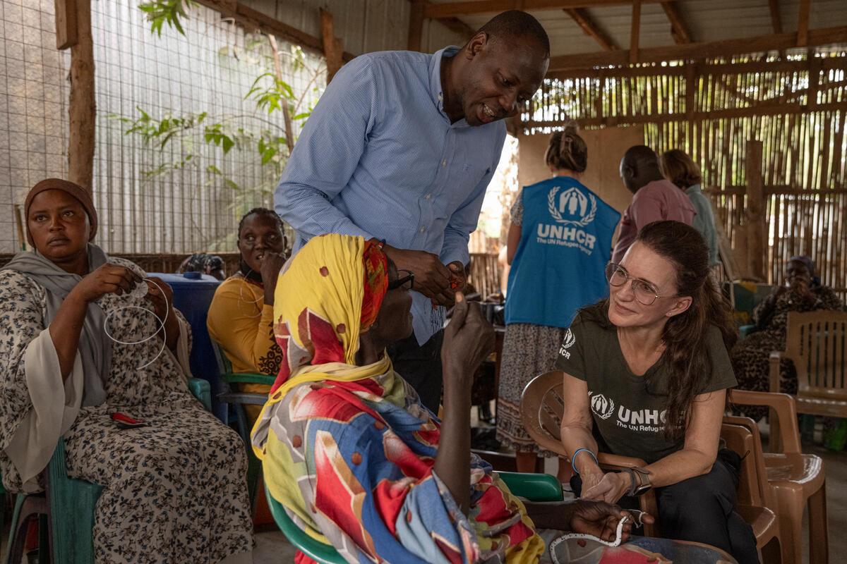 Kristin Davis listens as The Roots Project coordinator Malish Godfrey (middle) speaks with an elderly South Sudanese participant. They are inside a shelter and others are gathered behind them, nearby.