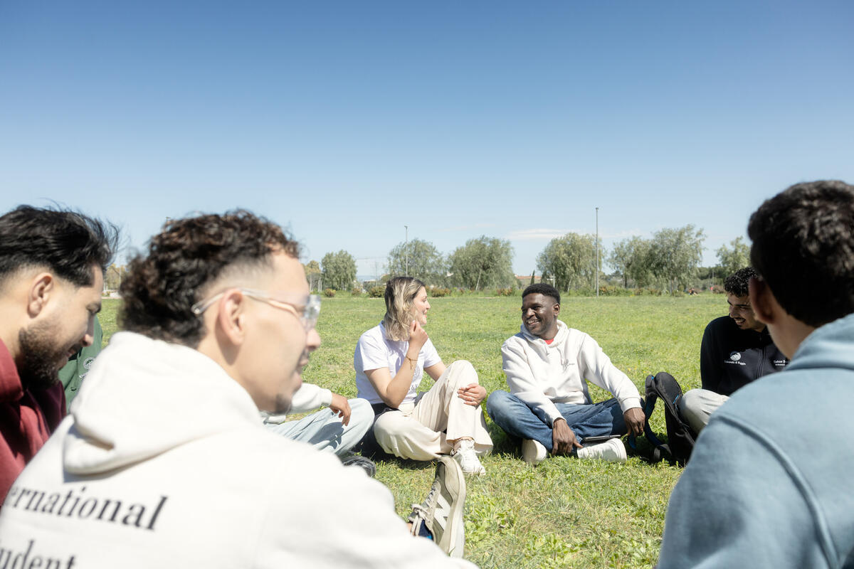 A group of people sit in a circle on the grass lawn of a park under a blue sky