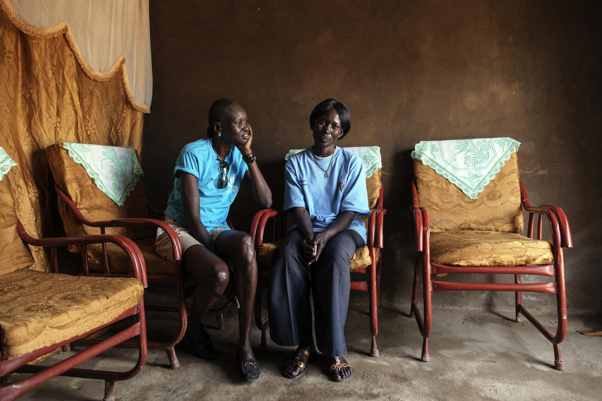 Two women sit next to each other on chairs.