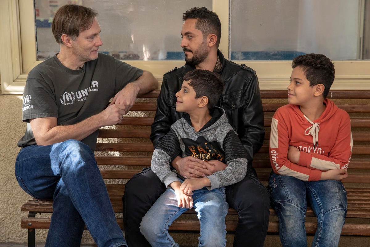 David Morrissey sits on a bench next to Abbas and his two sons.