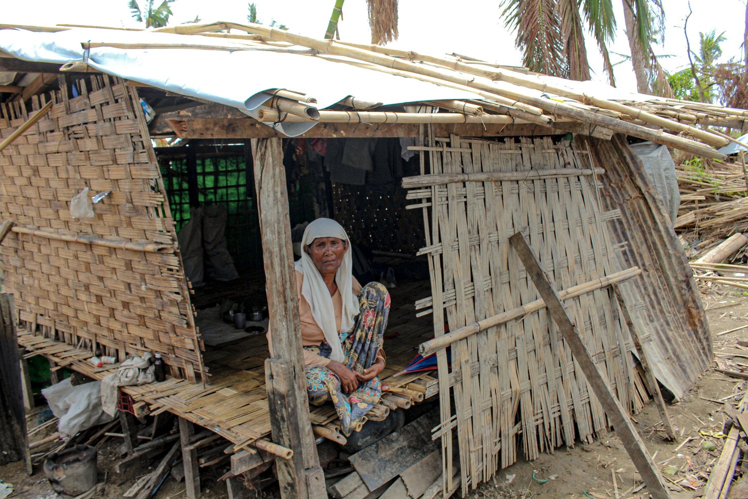 A woman sits in a makeshift bamboo shelter.