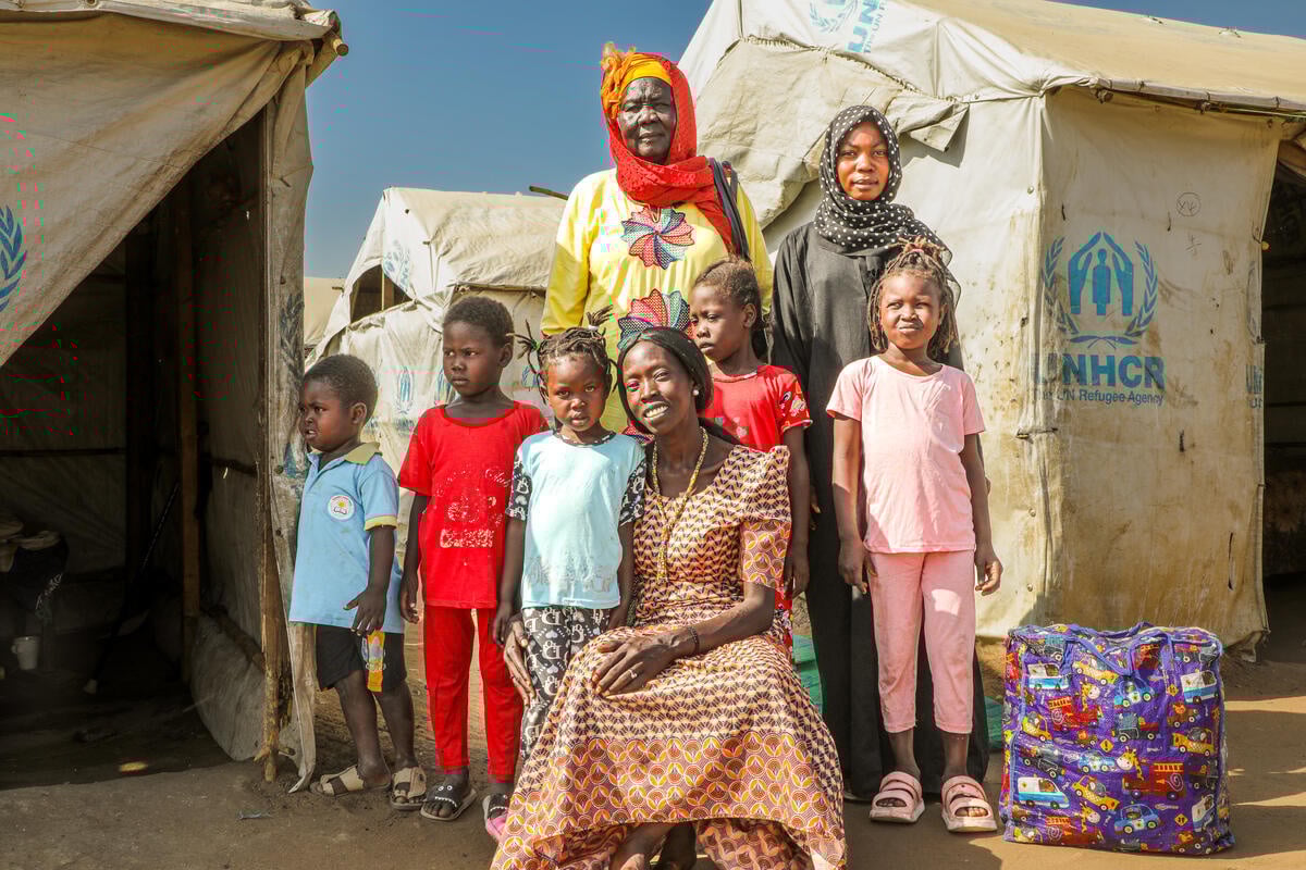A woman stands with her children and grandchildren outside in front of a UNHCR tent