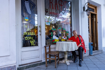 A smiling woman seated at a table in front of a café with colorful paintings on the windows and doors.