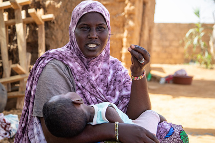A woman in a purple headscarf holding her sleeping child.