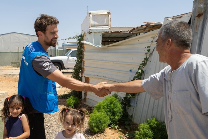 Two men are shaking hands while two young girls smile at the camera.